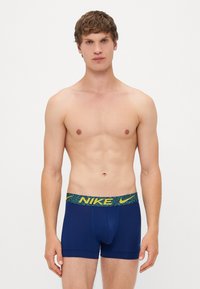 Marineblå boxer briefs med et struktureret grønt og gult bælte, der har Nike-logoet. Stoffet ser glat og tætsiddende ud, uden mønstre.