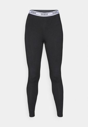 Black leggings with a fitted design, made from stretchable fabric. Features a white waistband with "GUESS" logo. Smooth texture, no patterns.