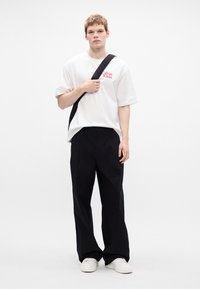 Tricou alb supradimensionat cu logo-ul roșu "Calvin Klein", asortat cu pantaloni largi negri și adidași albi. Design simplu și modern.