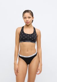 Μαύρο βαμβακερό αθλητικό σουτιέν με επαναλαμβανόμενο μοτίβο λογοτύπου CK και ζώνη με το εμπορικό σήμα, σε συνδυασμό με μαύρο σλιπ με λευκή λωρίδα λογοτύπου.