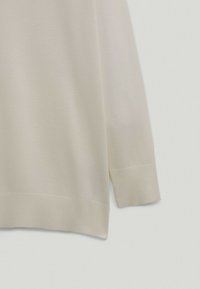 Ljust beige stickad tröja med lös passform, med långa ärmar och ribbat knäpp. Texturen är jämn med ett konsekvent stickmönster.