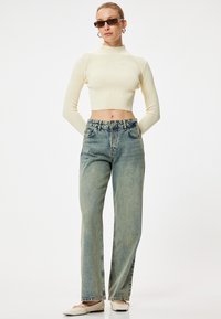 Top crema a coste, tagliato, jeans di denim azzurro chiaro a vita alta con gamba dritta, abbinati a scarpe basse chiare e occhiali da sole rettangolari.