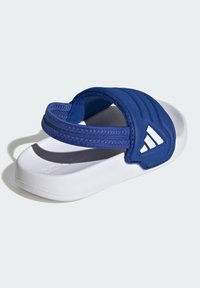 Sandalia blanca tipo chancla con una gruesa correa acolchada azul que presenta un logotipo de Adidas, sobre un fondo claro y liso.