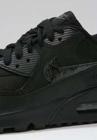 Detailní záběr na černé tenisky Nike Air Max, který zobrazuje strukturované tkaničky, síťované a kožené panely a viditelnou jednotku Air Max v podrážce.