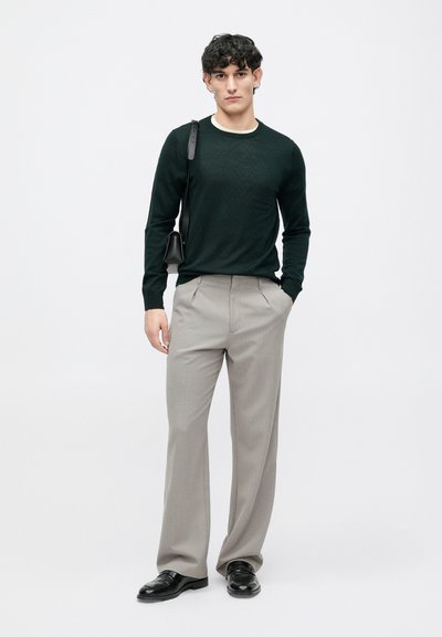 Dark green knit sweater with diamond pattern, paired with light grey pleated trousers. Black leather shoes and a small black shoulder bag.