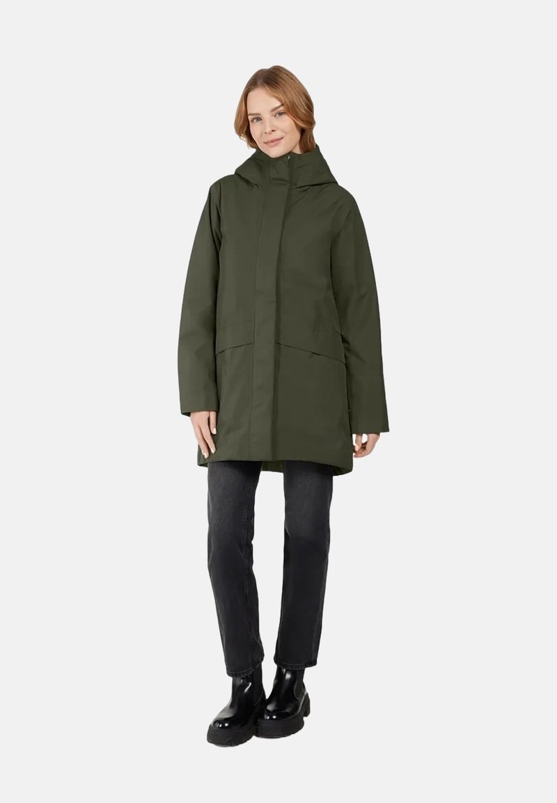 Olivgrüner, wasserdichter Mantel mit Kapuze, zwei vorderen Taschen und geradem Schnitt. Getragen über dunklen Hosen und schwarzen Stiefeletten.
