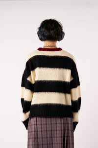 Pulover tricotat supradimensionat în dungi negre și crem, cu guler roșu, tiv dublu și umeri căzuți, purtat peste o fustă în carouri.