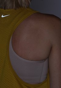 Canotta atletica gialla con texture in rete, con un logo Nike bianco sul retro, indossata sopra un reggiseno sportivo beige.