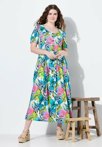 Kwiatowa sukienka maxi w intensywnych odcieniach niebieskiego, zieleni i różu z krótkimi rękawami, zapięciem na guziki z przodu oraz dopasowanym pasem. Noszona z sandałami na platformie.