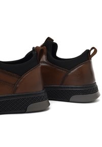 Chaussures en cuir marron avec une semelle noire texturée, dotées de languettes, d'un design bas à la cheville et de détails noirs contrastants sur le dessus.