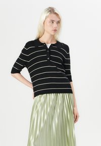 Polo nero a righe con colletto e apertura con tre bottoni, abbinato a una gonna plissettata in satin verde chiaro.