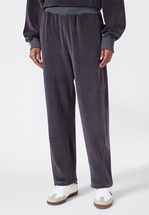 Jogging en velours gris avec une taille élastique, des poches latérales et une coupe décontractée, assortis à des baskets blanches avec des accents gris.