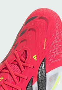 Chaussure de sport rouge avec une tige en mesh texturé, des accents noirs et des détails jaunes. Le design comprend plusieurs trous de ventilation et des lacets plats.