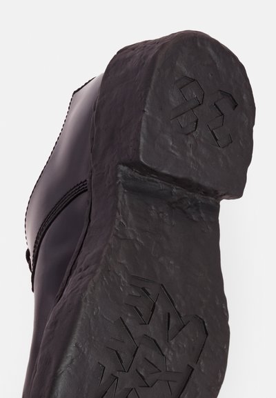 Black boot with a thick, textured rubber sole featuring a rugged design and embossed details. Smooth leather upper with stitching visible.