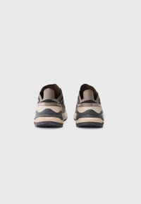Buty sportowe w beżowo-czarnym wzorze, z fakturowaną cholewką, wyściełaną podeszwą i wyraźnym logo na pięcie.