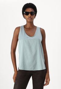 Lys blå tanktop med rund hals og afslappet pasform, fremstillet af et glat, blødt stof, parret med sorte, vinklede solbriller.