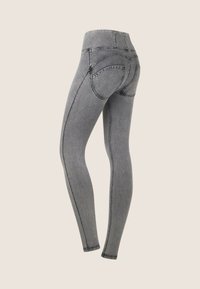 Harmaat korkeavyötäröiset farkkutrikoot, joissa on takana paikkataskut, näkyvät saumat ja kapea istuvuus nilkkoihin asti yksinkertaisella taustalla.