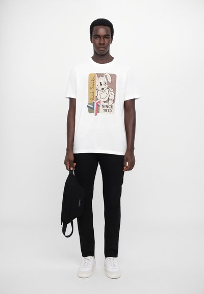 Balta kokvilnas T-kreklu ar krāsainu grafiku, kurā attēlots karikatūru zaķis ar uzrakstiem "Paul Smith" un "SINCE 1970", kombinēts ar melnām biksēm un plecu somu.