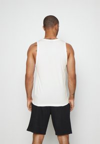 Biała bawełniana koszulka na ramiączkach z okrągłym dekoltem, bez rękawów, o luźnym kroju, zestawiona z czarnymi szortami. Gładka faktura, bez wzorów.