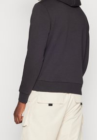 Felpa in cotone misto grigio scuro, con una vestibilità comoda, polsini e orlo a costine, abbinata a pantaloni cargo beige con tasche laterali.