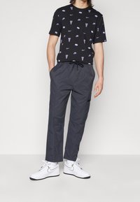 Zwarte katoenen t-shirt met verspreide Nike-logo's en de tekst "Just Do It". Gecombineerd met donkergrijze joggingsbroek met trekkoord en witte sneakers.