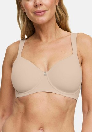 Vrouw draagt een beige beha met volledige bedekking, brede bandjes en een klein metalen hangertje middenvoor.