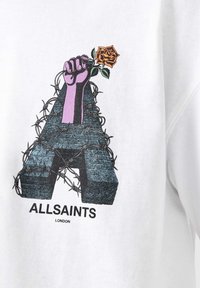 Den hvide sweatshirt har et stort grafik af en lilla næve, der holder en orange rose, indviklet med pigtråd omkring et stiliseret bogstav "A".