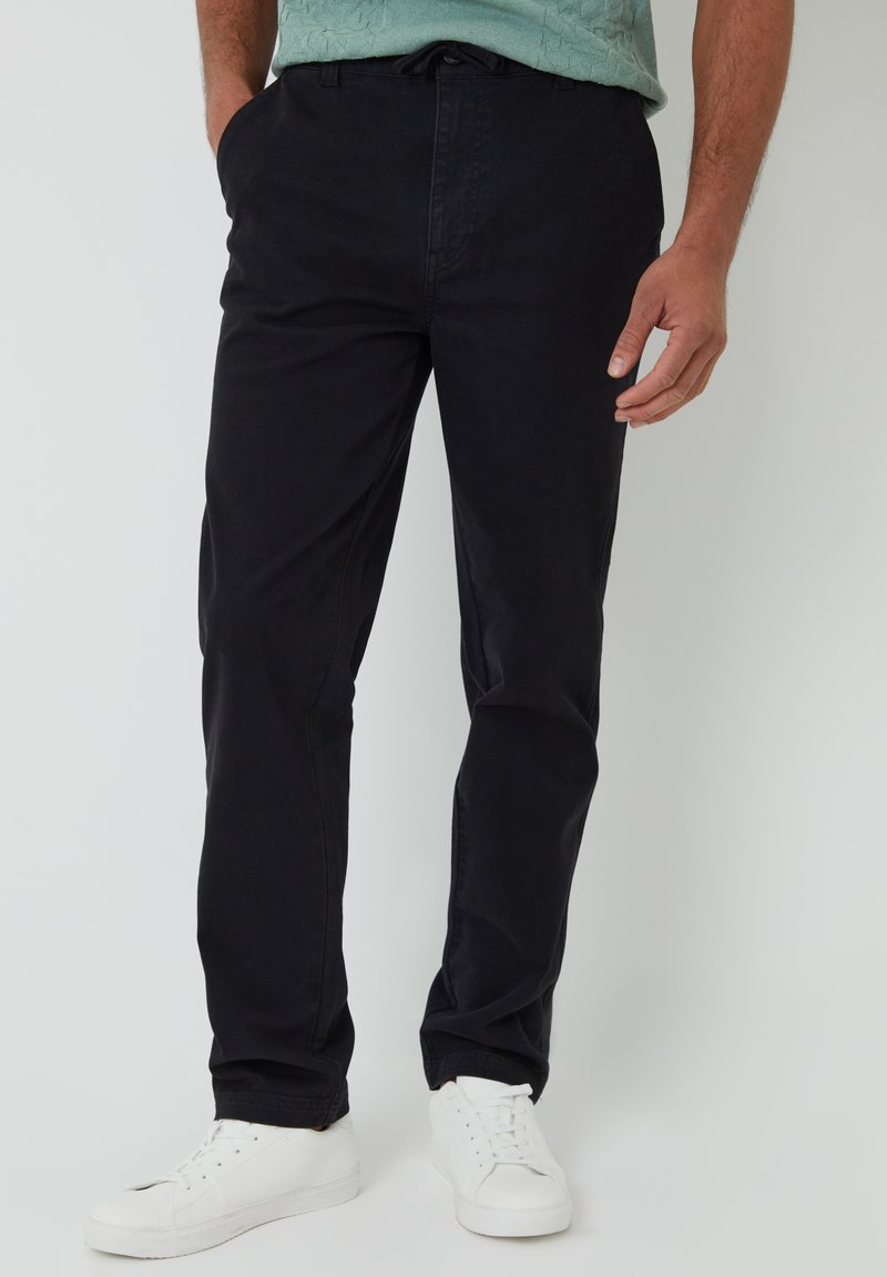 Chinos negros de algodón, con diseño de pierna recta, bolsillos laterales y traseros, combinados con zapatillas blancas.