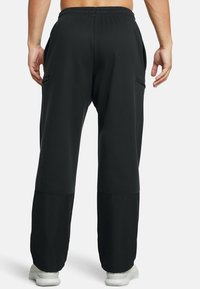 Črne široke hlače s elastičnim pasom, stranskimi žepi in manšetami. Narejene iz mehkega, trpežnega materiala z gladko teksturo.