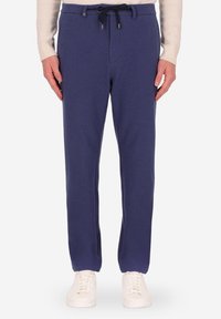 Pantaloni della tuta blu navy in morbido tessuto, con vita elastica e cordoncino e polsini affusolati. Abbinati a sneaker bianche.