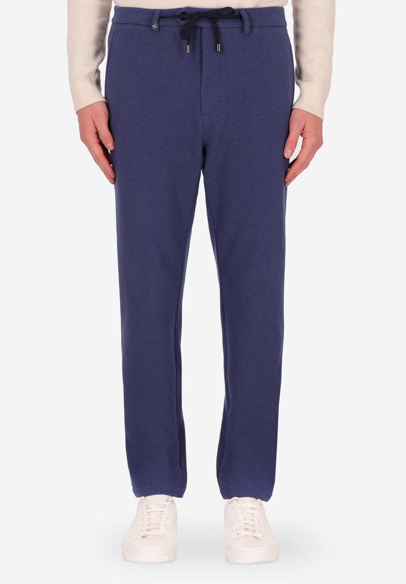 Pantaloni della tuta blu navy in morbido tessuto, con vita elastica e cordoncino e polsini affusolati. Abbinati a sneaker bianche.