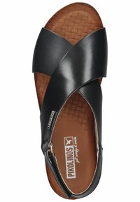 Sandalia de cuero negro con tiras entrelazadas, plantilla texturizada marrón y una plantilla acolchada. Presenta una pequeña etiqueta con el logo en el costado.