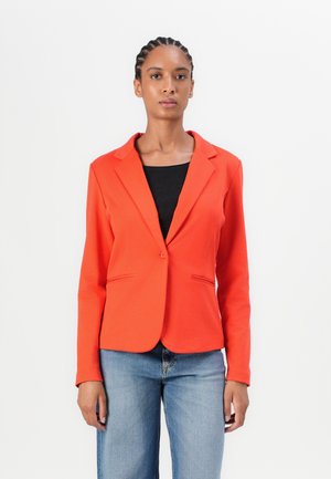 Rode blazer met een gesneden kraag, enkele knoopsluiting en twee voorkruiszakken. Fitted ontwerp, gecombineerd met een donkere top en blauwe jeans.