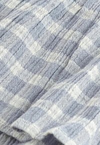 Tessuto blu chiaro con texture a motivo quadrettato, caratterizzato da quadrati alternati chiari e più scuri, che mostra un aspetto morbido e intrecciato.