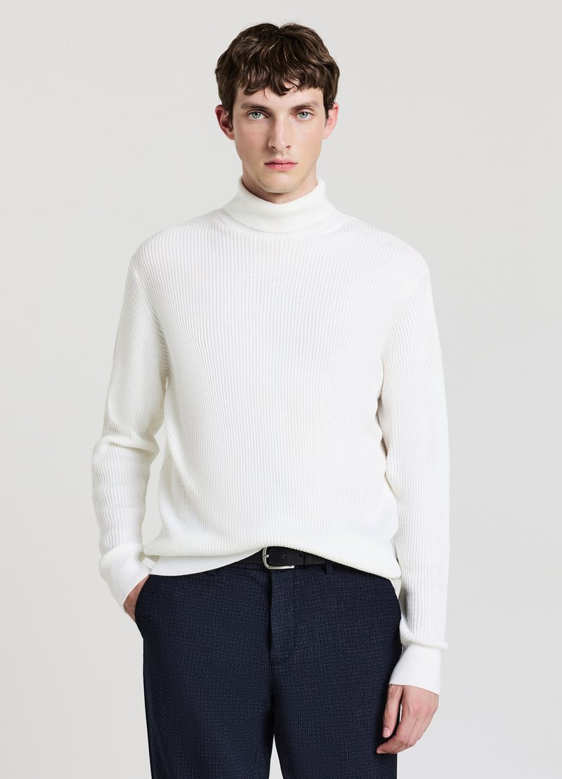 Maglione bianco a coste con collo alto e maniche lunghe, abbinato a pantaloni blu navy con trama e cintura nera. Design e vestibilità semplici e moderni.
