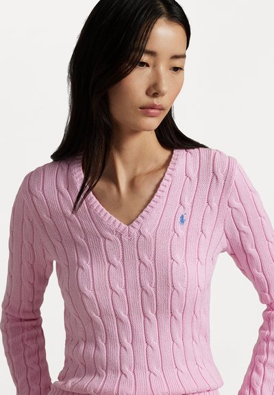 Pink cable knit sweater with a V-neck, featuring a small blue logo on the left chest. Long sleeves and textured pattern throughout.
