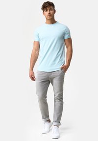 Camiseta ajustada azul claro de algodón, combinada con jeans de mezclilla gris enrollados y zapatillas blancas, que muestran un diseño simple y limpio.