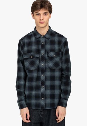 Black and blue plaid flannel shirt with long sleeves, two front pockets, and button closure. Textured fabric with a checkered pattern.