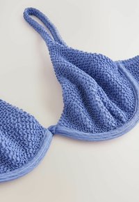 Plavi teksturirani bralette s volanima, podesivim naramenicama i glatkim donjim dijelom. Tkanina ima mekan, rastezljiv izgled.