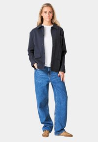 Mørkeblå jakke med krave, knaplukning og to forlommer, sat sammen med løst siddende blå jeans og lysebrune sko.