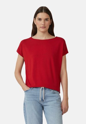 Rode, kortemouwtop met een relaxte pasvorm en brede ronde hals, gemaakt van zachte stof, gecombineerd met lichtgekleurde jeans.