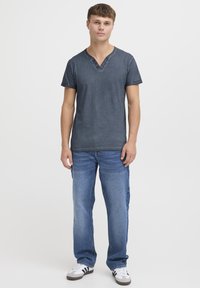 Mørkegrå T-skjorte med kort erme og V-hals, med tre knapper, kombinert med blå rettbukser og hvite joggesko med svarte striper.