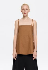 Top corto quadrato marrone con spalline sottili e regolabili, realizzato in tessuto testurizzato; abbinato a pantaloni neri a gamba larga. Design minimalista.