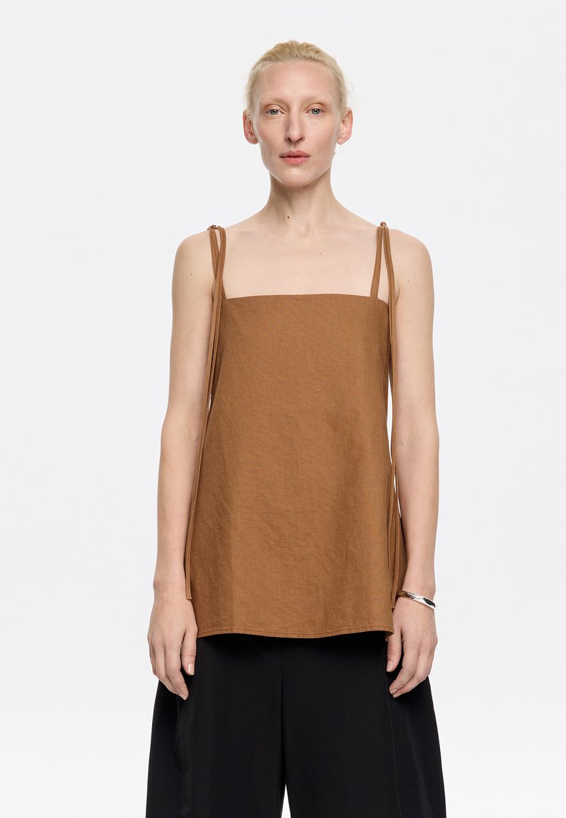 Top corto quadrato marrone con spalline sottili e regolabili, realizzato in tessuto testurizzato; abbinato a pantaloni neri a gamba larga. Design minimalista.