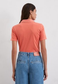 Koraalkleurig poloshirt met een kraag, korte mouwen en een gladde textuur, gecombineerd met lichtblauwe denim broek met hoge taille en achterzakken.