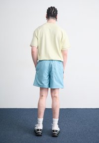 Camisa amarela-clara de manga curta, calções azuis com um cós elástico, socks brancas e ténis pretos com detalhes coloridos.