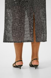 Rochie neagră cu paiete, cu o fante în spate, având un design transparent și o formă dreaptă. Pălărie cu toc kitten în culoarea verde măsliniu.