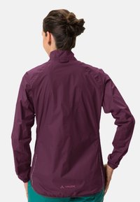 Veste légère bordeaux avec un col haut, des poignets élastiques et une finition imperméable. Présente un branding subtil et un design épuré.