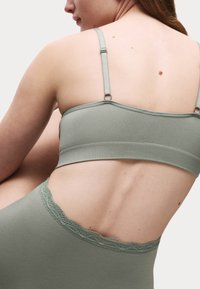 Bralette verde a costine con spalline regolabili e bordo in pizzo lungo il margine inferiore. Texture liscia e design corto per un look aderente.