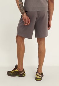 Gray athletic shorts with a smooth texture, featuring side pockets. Paired with brown and yellow running shoes with colorful accents.
